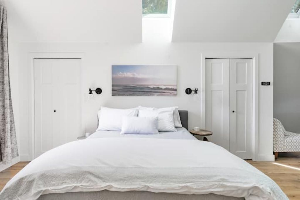 A bedroom with a large bed, two doors, a small table, and a painting on the wall.