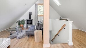 Una moderna camera da letto mansardata con soffitto spiovente, una scala a scomparsa, un'ampia finestra e un'accogliente angolo relax con divano e tavolino.