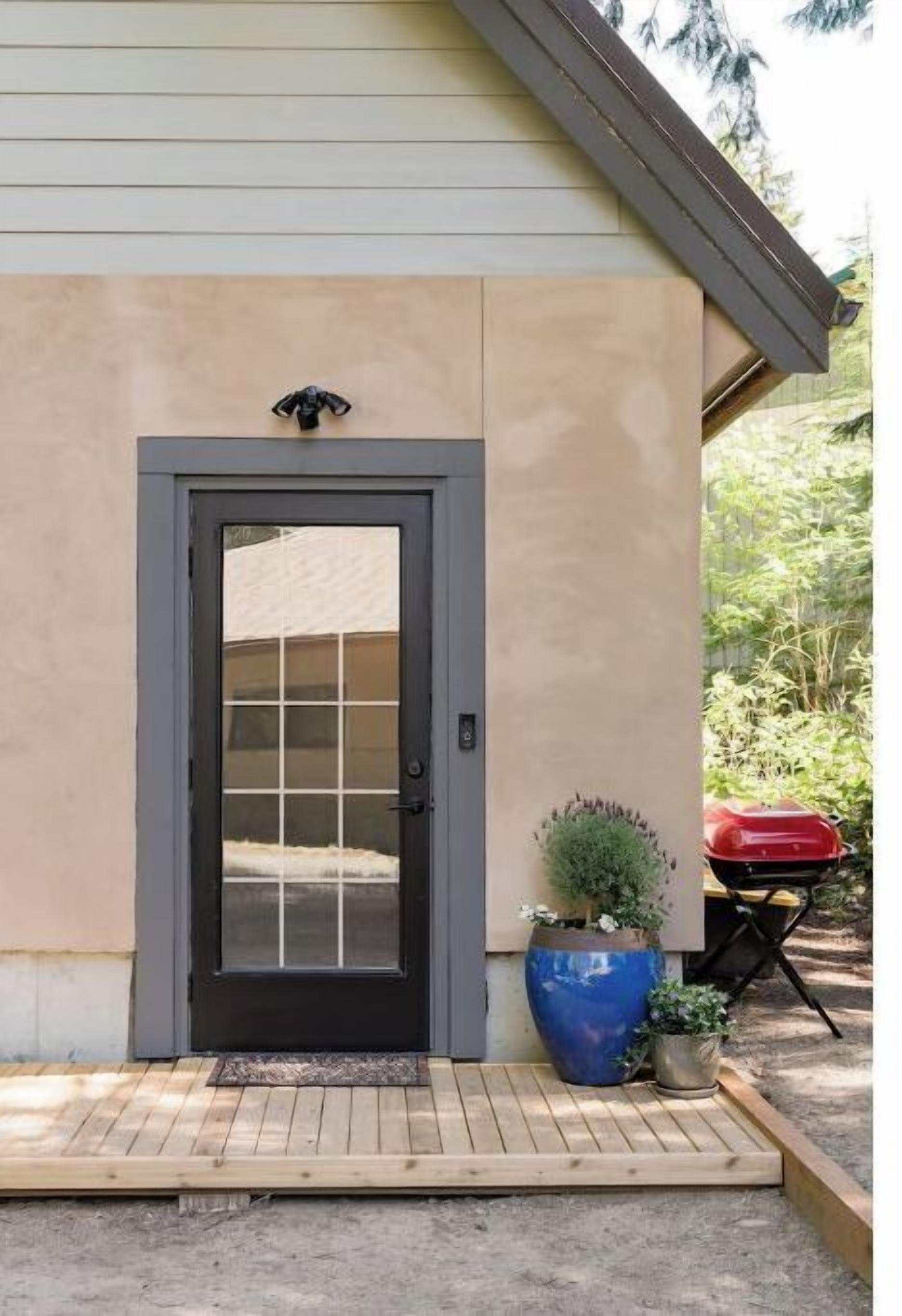 Una casa con puerta principal gris oscuro, un pequeño porche, una maceta azul y una parrilla roja.