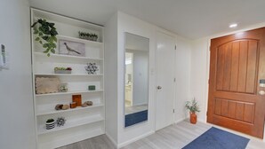 A hallway with a white wall, a wooden door, and a blue rug.
