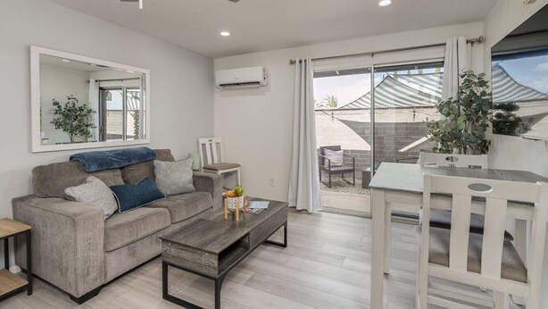 A modern living room with a grey sofa, a wooden coffee table, and a dining area with a white table and chairs.