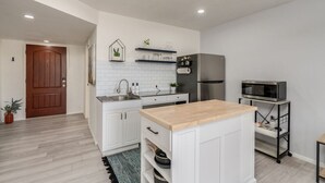 A modern kitchen with white cabinetry, a stainless steel refrigerator, a microwave, and a wooden countertop.