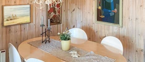 Een kamer met houten lambrisering, een ronde eettafel, witte stoelen, een kroonluchter, een schilderij en een potplant.