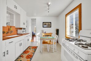 Cozinha compacta com armários brancos, micro-ondas, fogão e um espaço de refeições com mesa e cadeiras.