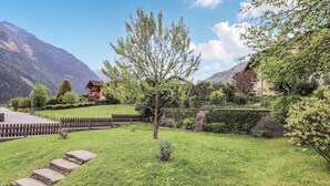 A rural landscape with a wooden fence, a small tree, and a stone pathway leading to a house with a sloped roof.