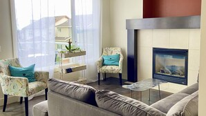 A living room with a sofa, two armchairs, a small table, a fireplace, and a large window with curtains.