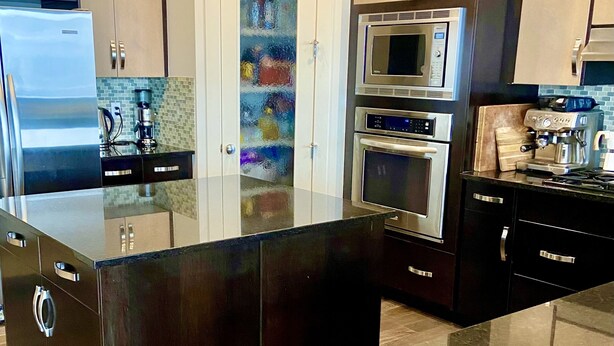 A modern kitchen with stainless steel appliances, dark cabinetry, and a glass backsplash.