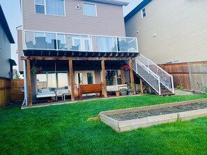 Une maison à deux étages dotée d’un patio couvert, d’une terrasse en bois et d’un petit jardin.
