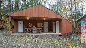 A rustic cabin with a covered outdoor seating area, a table, and two doors.