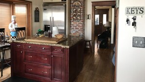 A kitchen with a central island, wooden cabinets, a stainless steel refrigerator, and a brick accent wall. - The Center of Vancouver, Spacious Elegant Interior, Spectacular Outdoor Living (Vancouver)