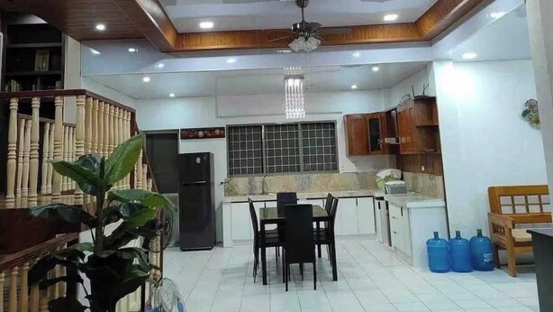 Un vaste espace de vie comprenant un coin repas avec une table, une cuisine dotée de meubles en bois et un ventilateur de plafond.