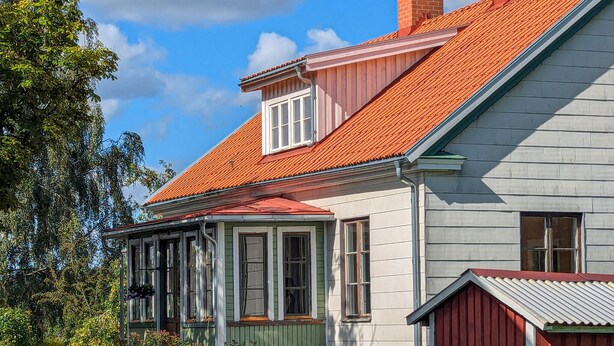 Een tweelaags huis met een rode dakbedekking, een dakvenster en een klein bijgebouw met een rood dak.