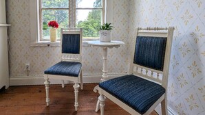 Twee retro fauteuils met blauwe kussens en een bijzettafeltje met een potplant, voor een behangwand met een raam op de achtergrond.