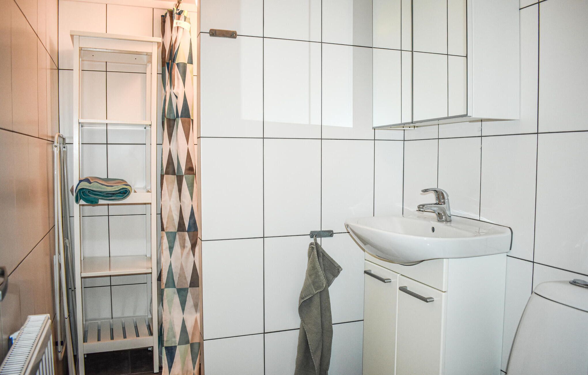 A bathroom with a white sink, a towel rack, and a shower area with a patterned curtain.