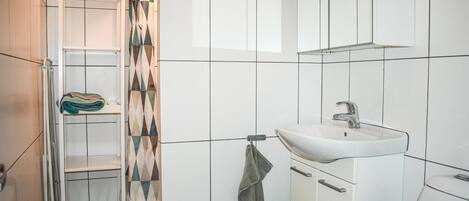 A bathroom with a white sink, a towel rack, and a shower area with a patterned curtain.