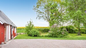 Une grange rouge avec une allée de gravier menant à une zone herbeuse agrémentée d’arbres et d’arbustes.