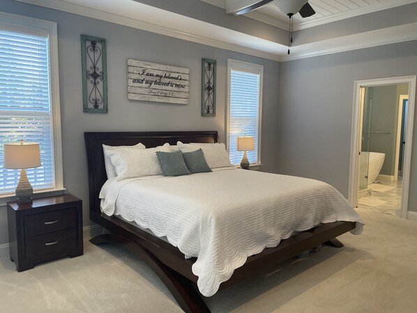 A bedroom with a large bed, two bedside tables with lamps, a dark wooden headboard, and two decorative wall pieces.