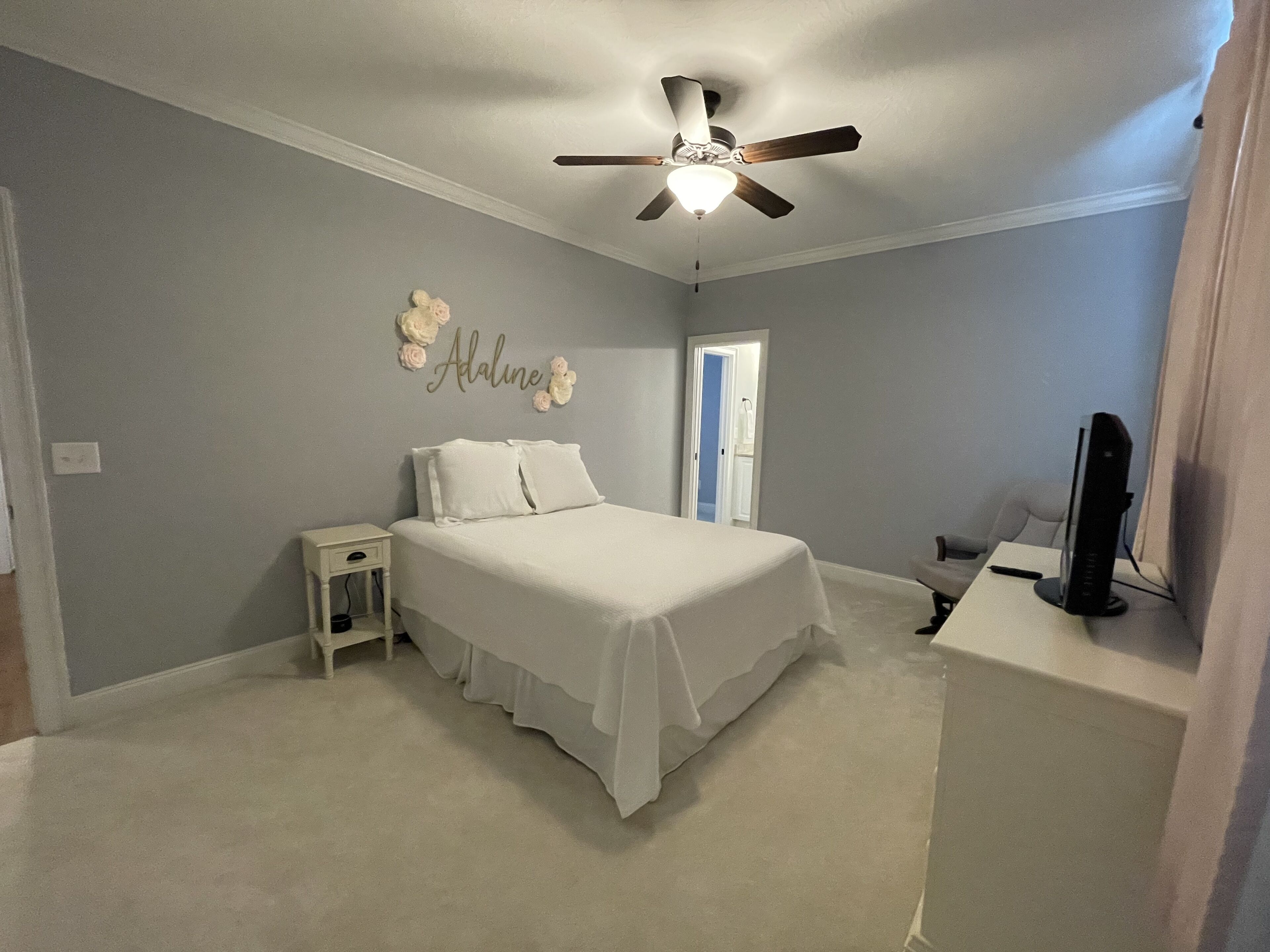 A bedroom with a bed, a nightstand, a ceiling fan, and a TV.