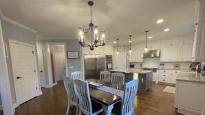 A modern kitchen with white cabinetry, a central island, and a dining area with a chandelier. - Perfect Masters Golf Rental Home - 12 miles from the Augusta National (North Augusta)