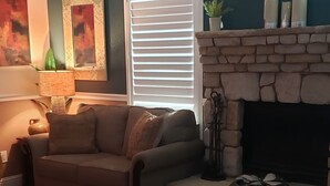 A living room with a stone fireplace, a sofa, a coffee table, and a lamp. - Colorful 2-bdr, 2-bth unique serenity. (Modesto)