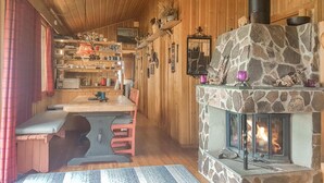 Ein gemütliches Blockhaus-Interieur mit Kamin aus Stein, Holzwänden und einer Essecke mit Bank und Tisch.