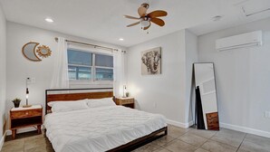 Una camera da letto con un letto, comodini, una ventola a soffitto, una finestra con persiane, uno specchio fissato alla parete e un condizionatore d'aria.