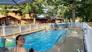 A swimming pool area with a white fence, lounge chairs, and a person sitting on a chair. - DRIFTWOOD RESORT BULL SHOALS (Bull Shoals)