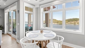 A dining area with a round table, white chairs, and a view of a river and hills.