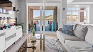 A modern living room with a sofa, coffee table, and a TV. There is a sliding glass door leading to a balcony with a view of the outdoors.