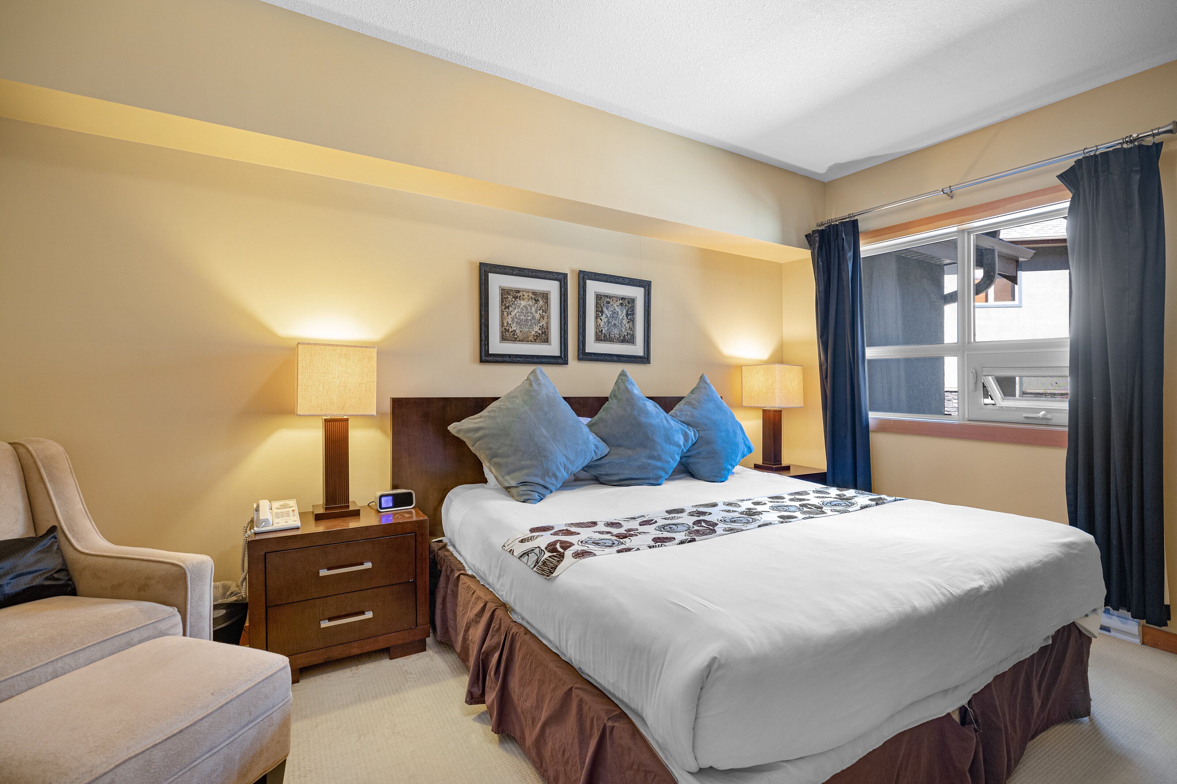 A hotel room with a large bed, two bedside tables, a chair, and a window with curtains.