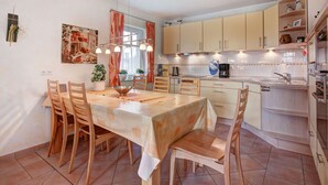 Una cocina moderna con comedor, que incluye una mesa grande, sillas de madera y una lámpara colgante.