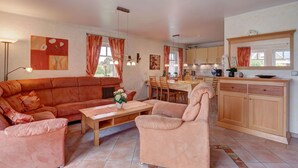 Una sala de estar con sofá, sillón y mesa de centro, un comedor con sillas y mesa, y una cocina con armarios y encimera.