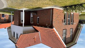 Un edificio de ladrillo de dos pisos con techo plano, balcón y una ventana con reja de metal.