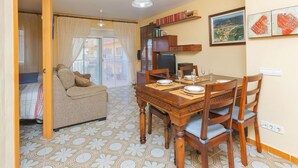 A dining area with a wooden table set for four, a sofa, and a TV in the background. - Beautiful apartment for 4 guests with WIFI, pool, TV and balcony (Santa Susanna)