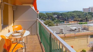 A balcony with a table and chairs, overlooking a coastal area with buildings and trees. - Beautiful apartment for 4 guests with WIFI, pool, TV and balcony (Santa Susanna)