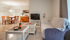 A living room with a sofa, a TV, a dining table with chairs, and a kitchen area in the background. - Nice apartment for 4 guests with WIFI, TV and terrace (Rijeka)
