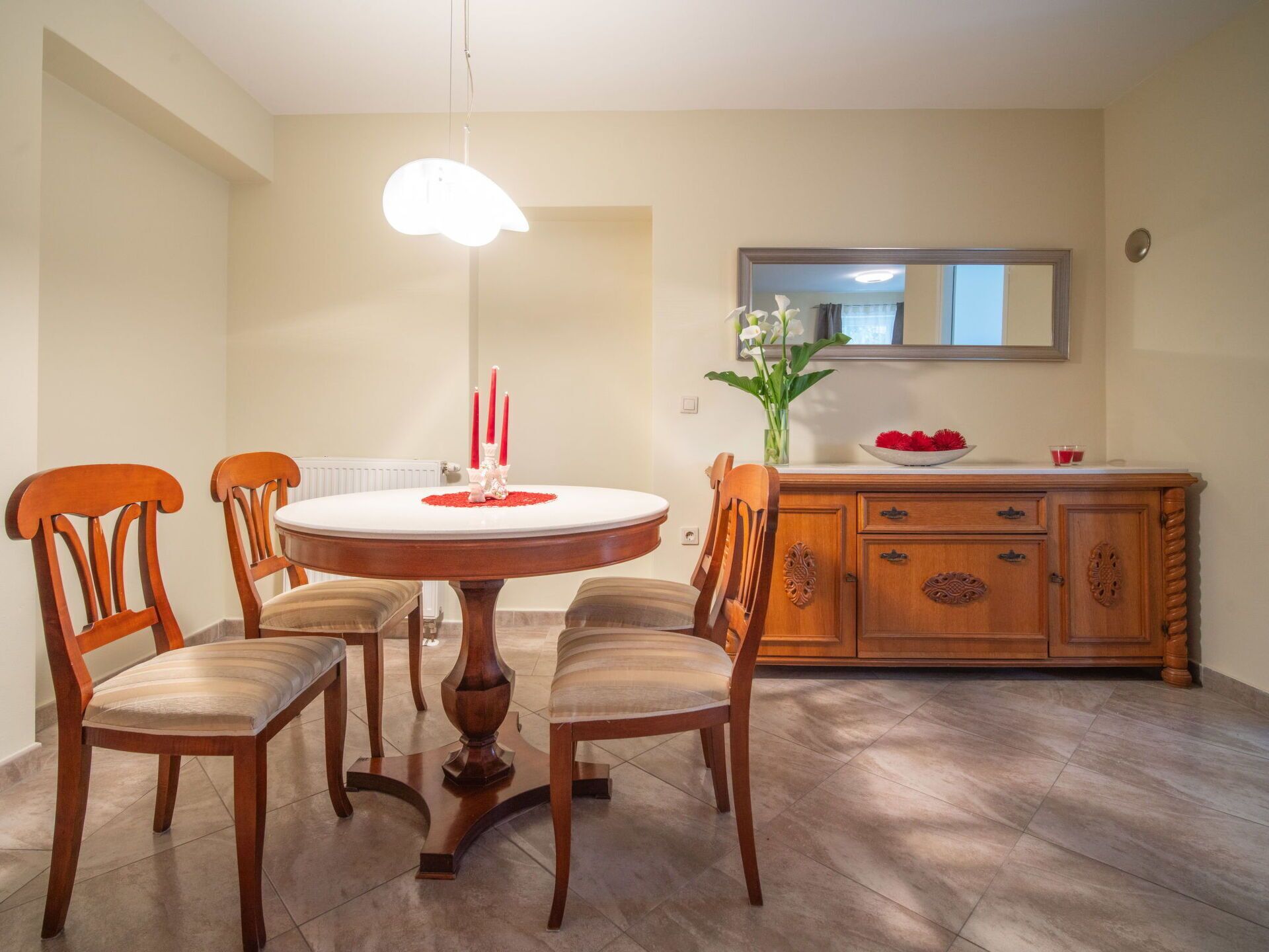 A dining area with a round table, four chairs, a wooden cabinet, and a mirror on the wall.