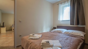 A neatly made bed with a brown quilt, a bedside table with a lamp, and a window with curtains. - Nice apartment for 4 guests with WIFI, TV and terrace (Rijeka)