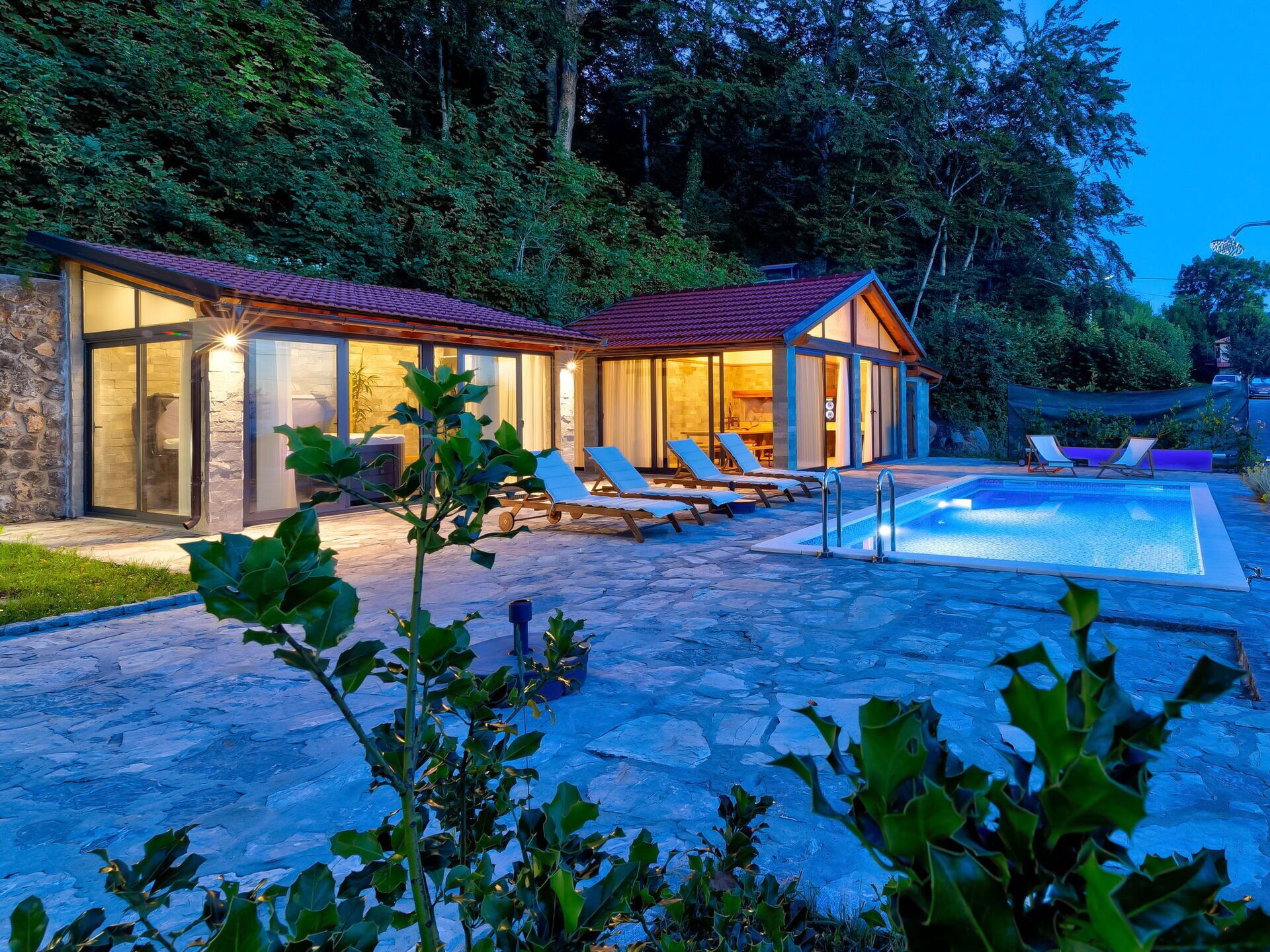 A modern house with a swimming pool, stone patio, and lounge chairs.