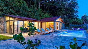 Ein modernes Haus mit Schwimmbad, einer Steinterrasse und Liegestühlen.