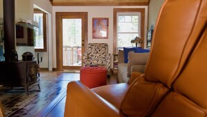 Una sala de estar acogedora con techo de madera, un reposapiés rojo y un sillón de cuero.