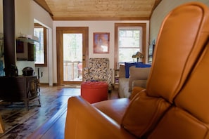 Una sala de estar acogedora con techo de madera, un reposapiés rojo y un sillón de cuero.