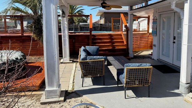 A covered outdoor seating area with two wicker chairs, a wooden deck, and a pool in the background.