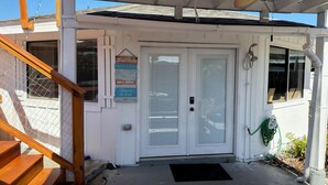 A covered porch with a wooden staircase, a white door with a glass panel, and a ceiling fan.