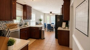 Una cocina con armarios de madera, salpicadero de azulejos y una zona de comedor con mesa y sillas.