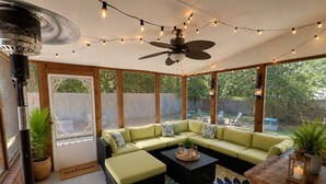 Un espacio exterior techado con una zona de estar modular, un ventilador de techo, luces colgantes y vistas al patio trasero.