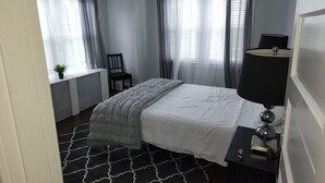 Une chambre à coucher avec un lit, une chaise, un bureau, une lampe et une fenêtre avec des rideaux.