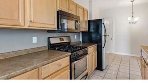 Une cuisine avec des meubles de rangement en bois, un réfrigérateur noir, une cuisinière et un four à micro-ondes.