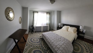 Quarto de hotel com cama, mesas de cabeceira, escrivaninha e janela com cortinas.