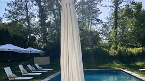 A poolside area with wicker chairs, a large umbrella, and a brick patio. - 5BR, Luxury Home, Pool, Large Yard , Close to Beach & Town (Southampton)